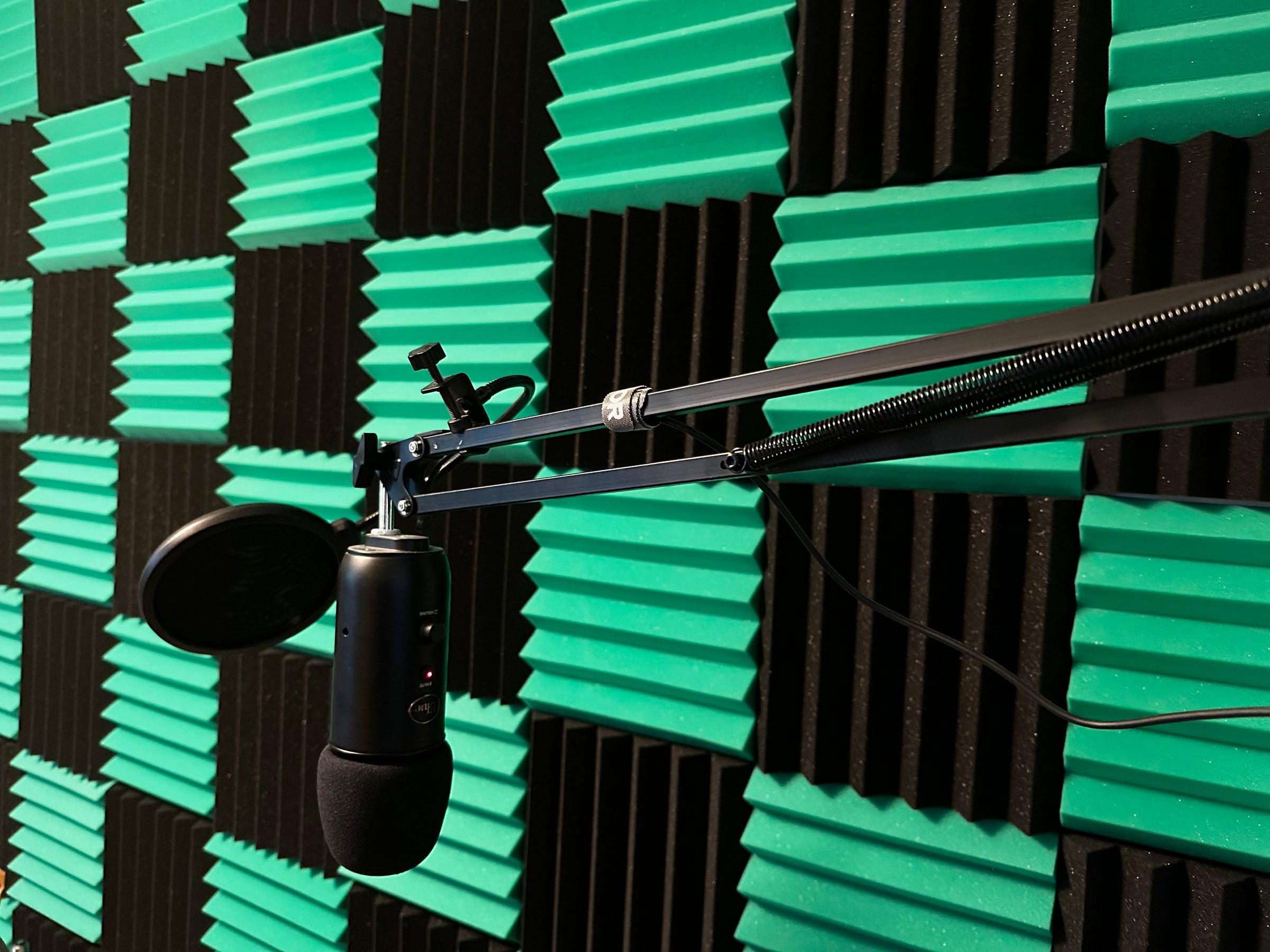 Checkerboard grid of sound insulation foam tiles on a wall with a professional arm-mounted microphone in front