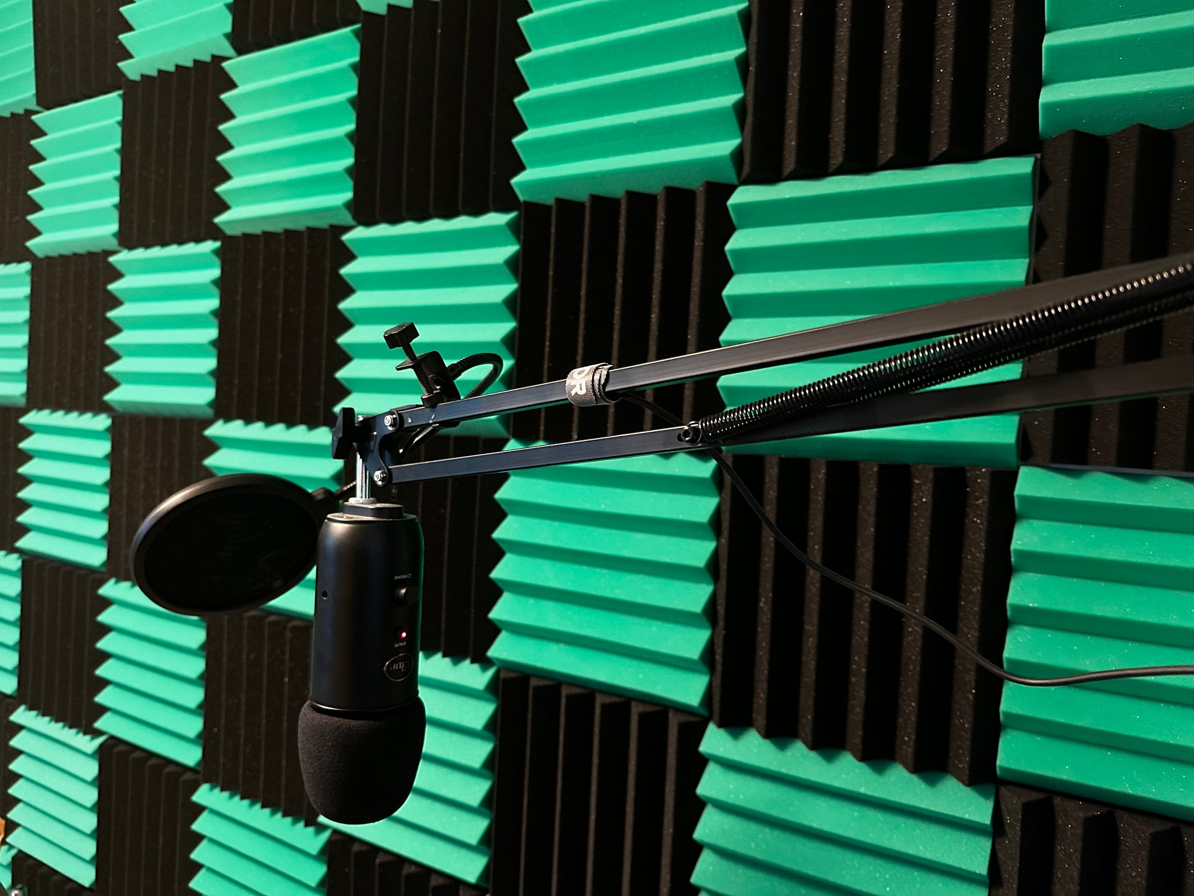 Checkerboard grid of sound insulation foam tiles on a wall with a professional arm-mounted microphone in front 
